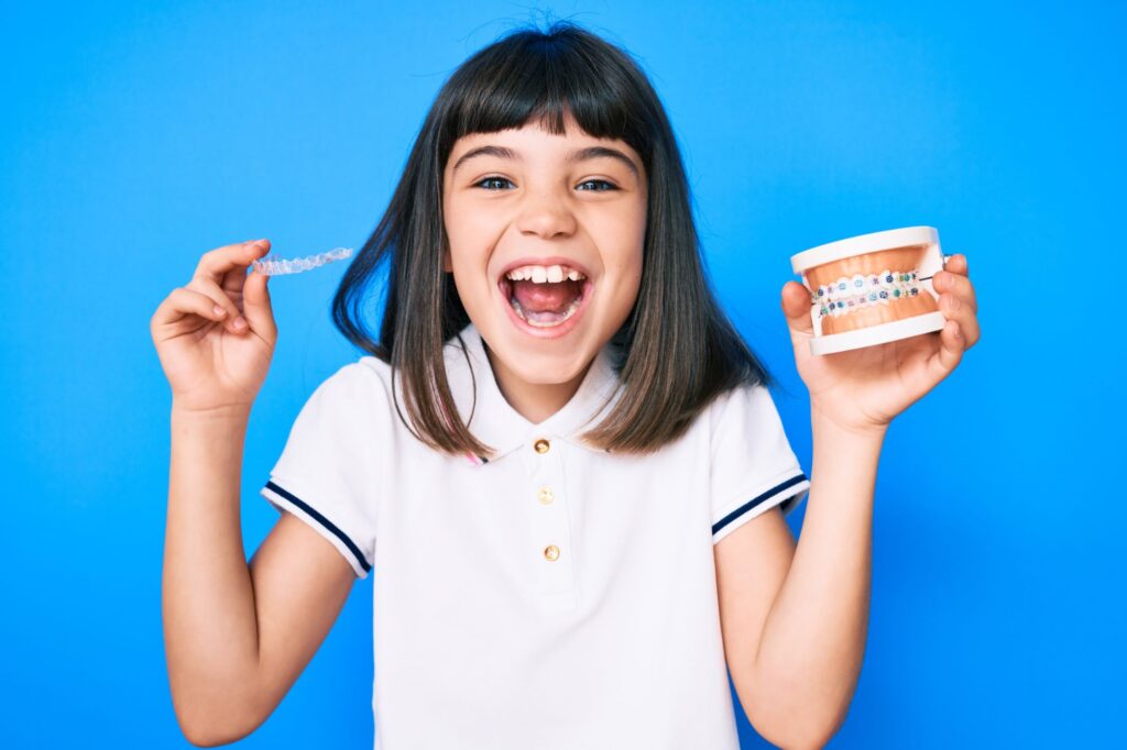 Girl holding a toothbrush and a model of teeth with braces