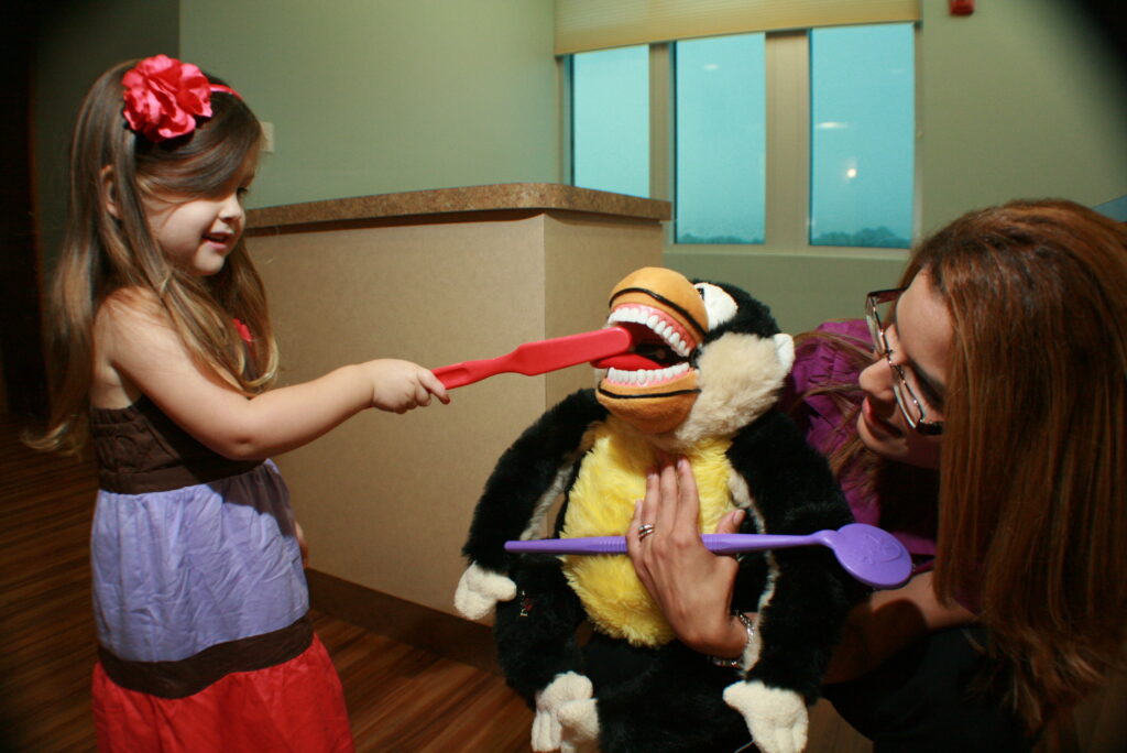 Kids learning to brush a puppet's teeth at our pediatric dental office