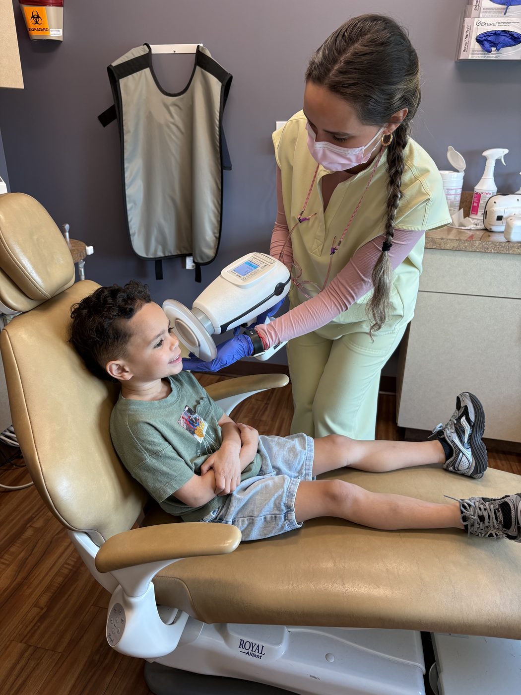 A smiling boy in the dental chair as the hygienist shows him the x-ray sensor